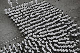 People marching in file and lining up for something that looks like a PT exercise in a military school