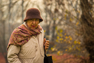 Photo of an old lady in a hat and raincoat on an autumnal day