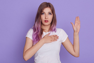 A photo of a young woman with her right hand on her heart and her left hand raised as though making an oath.