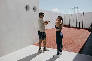 Two people in sports clothes stretch in an outside gym. Accompanies article with Corey Shader’s pro fitness tips.