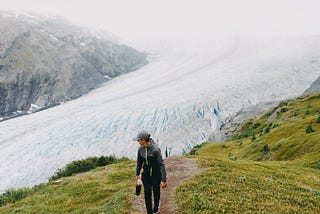 Lone individual, hiking uphill with a magnificent Alaskan glacier backdrop.