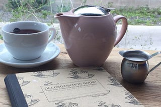 A teapot and tea cup with a writing notebook.