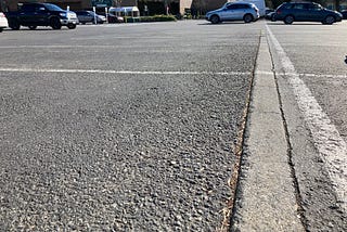 Close up of a strip of concrete in the asphalt parking lot with newer store in the background