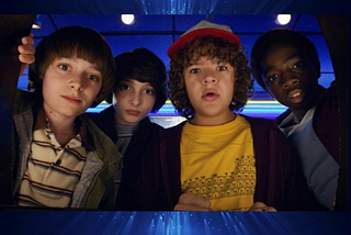 Four of the younger characters from Stranger Things looking down at the camera