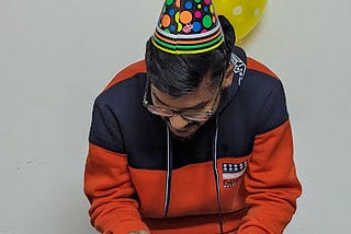 Me cutting a cake wearing a birthday hat and some decorations in the background