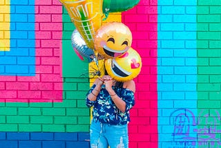 A young girl covering face with smiley balloons with colourful and vibrant background.