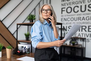 Fifty-year-old businesswoman with documents in her hand speaks on a mobile phone in a modern office