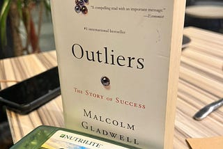 A copy of Outliers in front of a Double X