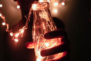 A boy holding a bottle filled with lights on a string