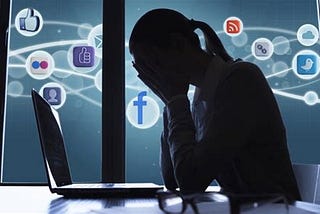 A person with their head in their hands. A laptop is in front of them, and various social media logos are in the background.