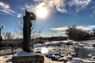A statue of a Native American gazes across a frozen river.