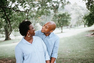 A middle age black couple hugging while outside in a garden.
