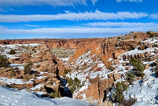 A rock canyon with snow clinging to the rocks and more snow in the foreground. Blue sky with streaks of white clouds.