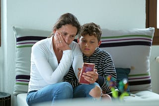 A photo of a mother and her young son looking at the phone with worried looks on their faces.