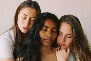 Three young women hugging, eyes closed. Photo from the shoulders up.