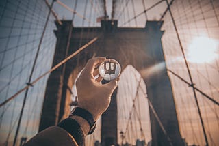 Hand holding glass ball up to the Brooklyn bridge. Glass ball shows bridge reflection but reversed.
