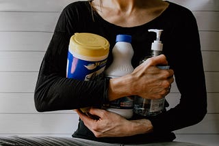 A woman holding 3 cleaning products in her arms