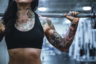 Photo of the torso and arm of a heavily tattooed woman lifting a weight