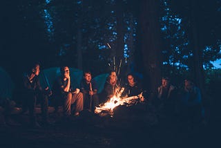 People huddled around a bonfire at dusk and telling stories