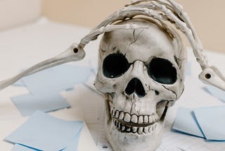 photo of a desk littered with post-it notes, with a model skull clutching its head with model skeleton hands as if in distress over all the post-it notes
