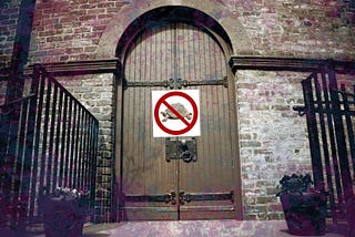 A large wooden door inside a gated building with a ‘no turtles allowed’ sign on top of it