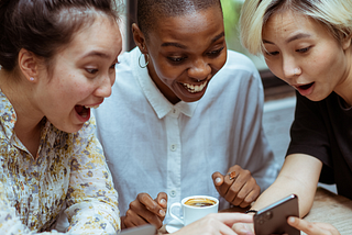 Fun group of three women looking surprised and excited by what they see on a phone