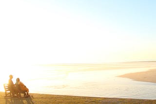 An old couple at sunset, having navigated life’s transitions, is still committed after a lifetime of relationship building.