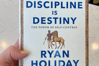 Discipline Is Destiny Book Cover in hand with a painted nail.