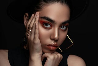 Woman wearing  make up and gold colored diagonal earrings. The dark background sets the stage for her mental state.