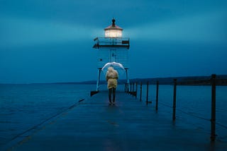 Person holding an umbrella on a pier near a lighthouse