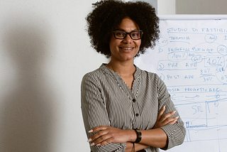 Black woman wearing glasses with curly afro standing with her arms crossed in front of a college chart.