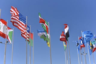 Multinational flags waving in the wind under a blue sky.