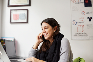 A woman sitting at a desk. She is smiling while talking on a mobile phone.