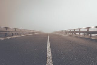 A concrete road under a gray sky leading into unknown