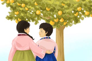 Two women in Korean hanboks stand in front of an orange tree looking at each other with one woman’s arm around the other.