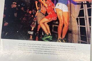 Photo of the band ‘JungK’ taken in NYC in 1998. There are four girls in the band dancing in brightly colored clothes and several photographers are taking their photo in a large room with a floor-to-ceiling window behind them.