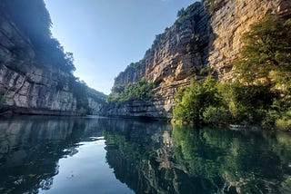 A narrow river gorge in France surrounded by high cliffs. The cliffs are lit on one side by a low sun, and sark on the other.