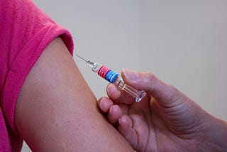 Syringe about to be used to inject vaccine into upper arm or patient.