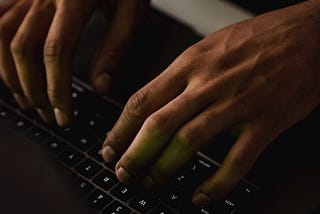 A dark hand typing away on a keyboard