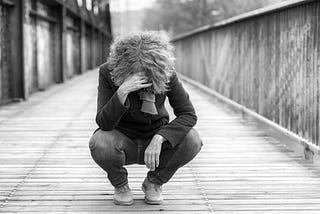 Dejected woman squatting on a bridge hanging her head with hand to her forehead outdoors on a cold day.