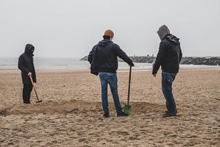 Three men building a sandcastle, or rather discussing it