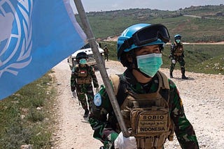 A UN peacekeeper with marching with a UN flag. https://peacekeeping.un.org/en