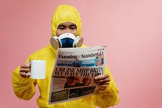 Dude in protective gear with coffee reads newspaper. For some reason the background is pink. It looks weird.