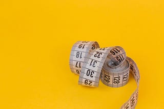 A coiled measuring tape rests against a solid yellow background