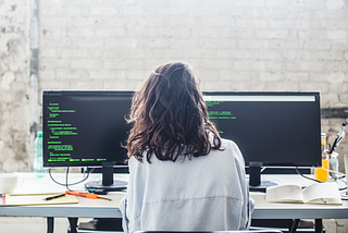 Woman software engineer coding at her desk using two monitors.