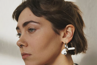 Woman wearing silver earrings with a single AirPod dangling from it.