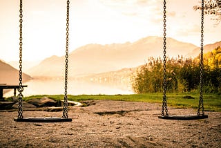 Two empty swings hanging side by side at sunset. Evoking a sense of absence, memory, and quiet reflection.
