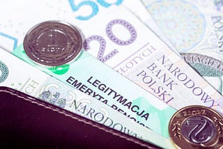 Na zdjęciu widoczne są polskie banknoty 20 i 50 złotych, monety oraz legitymacja emeryta-rencisty częściowo schowana w portfelu. Całość przywołuje skojarzenia z poczuciem finansowego wsparcia i bezpieczeństwa, jakie może zapewniać dodatek dopełniający. Zestawienie pieniędzy oraz dokumentu emerytalnego budzi wrażenie stabilności i spokoju, płynących z posiadania środków na codzienne potrzeby.