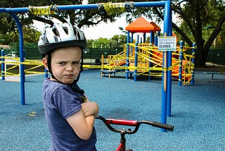 Boy with helmet and bike arriving at a closed playpark and expressing upset feelings.