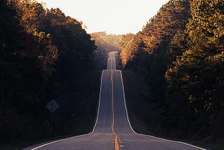 A road leading into rolling hills with lush trees growing on both sides